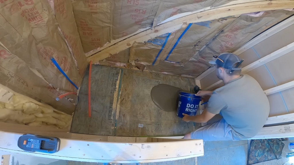 man pouring self-leveling compound into unfinished shower space area
