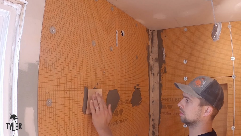 man applying Kerdi band to screw hole in wall of incomplete walk-in shower