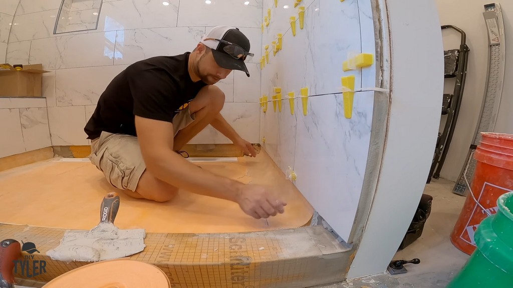 man applying Kerdi band to floor seams of walk-in shower