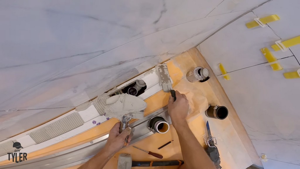 man applying mud to bottom piece of drain channel for walk-in shower