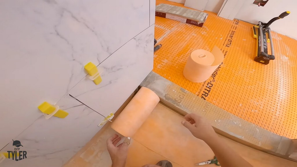 man applying Kerdi band for waterproofing walk-in shower curb