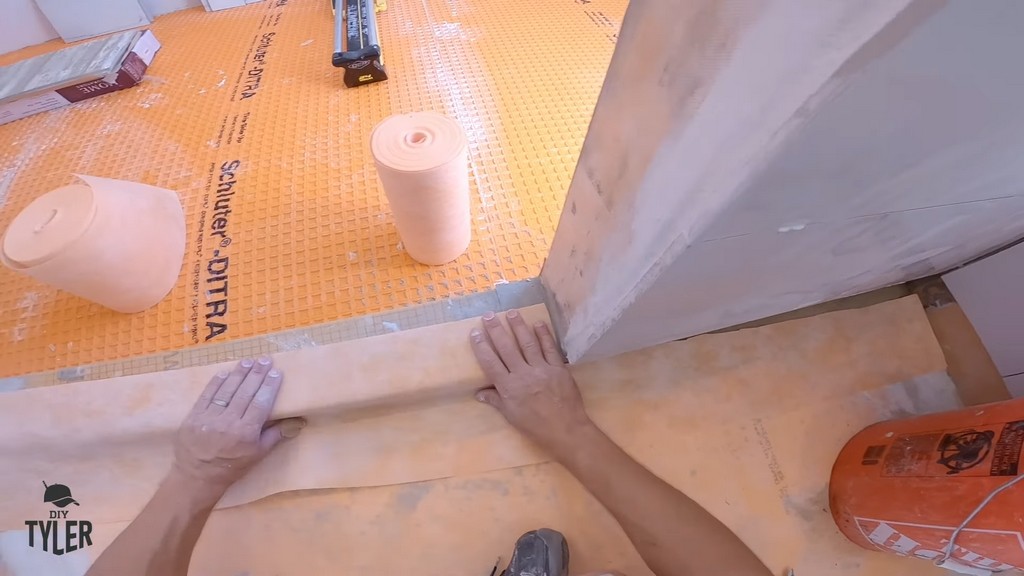 man applying Kerdi band to walk-in shower curb