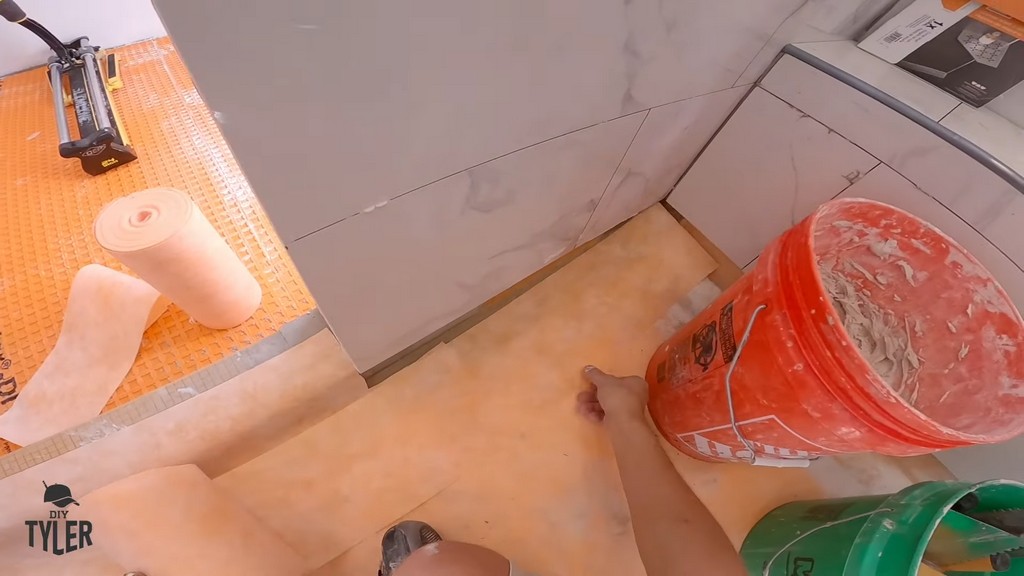 man applying Kerdi band to seam of walk-in shower floor