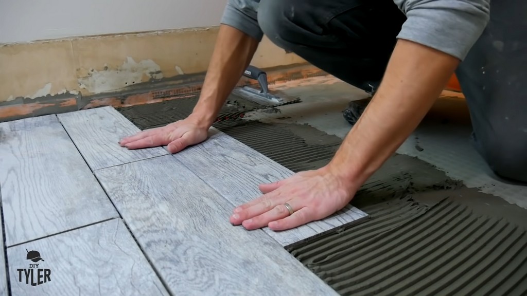 man applying pressure to piece of tile in bathroom