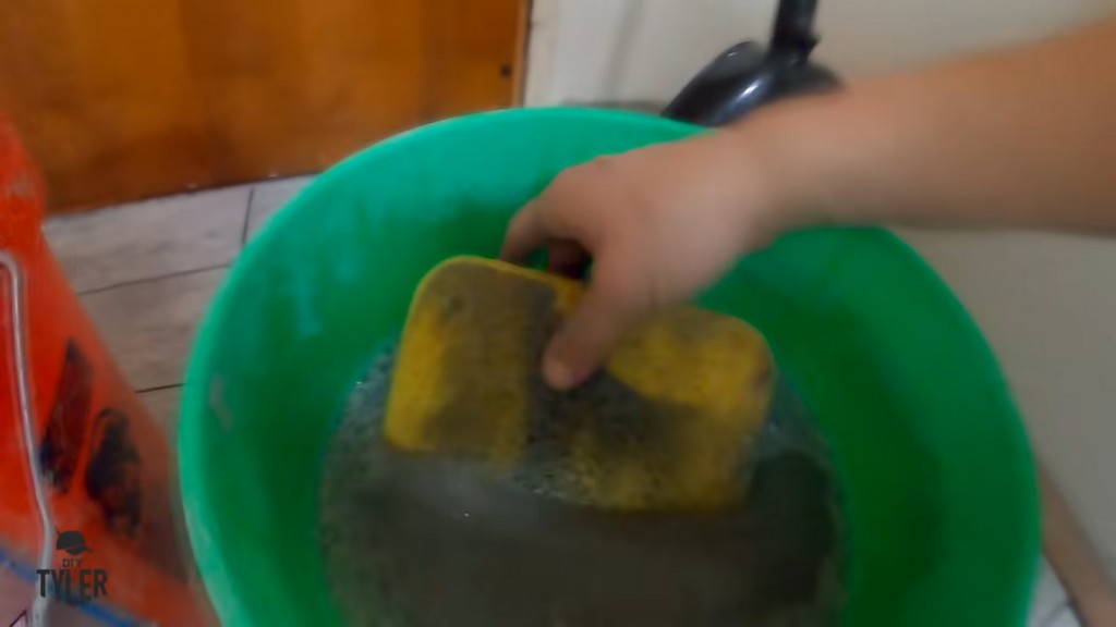 man cleaning grout off of sponge in bucket of water