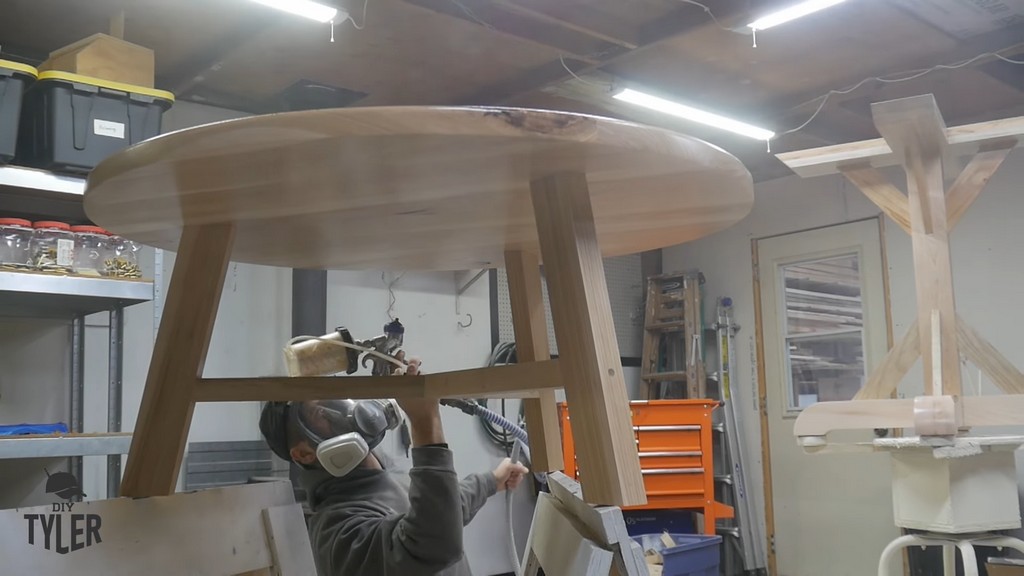 man applying spray finish to underside of DIY round coffee table