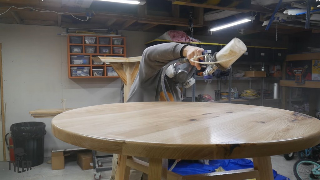 man applying spray finish to top of DIY round coffee table