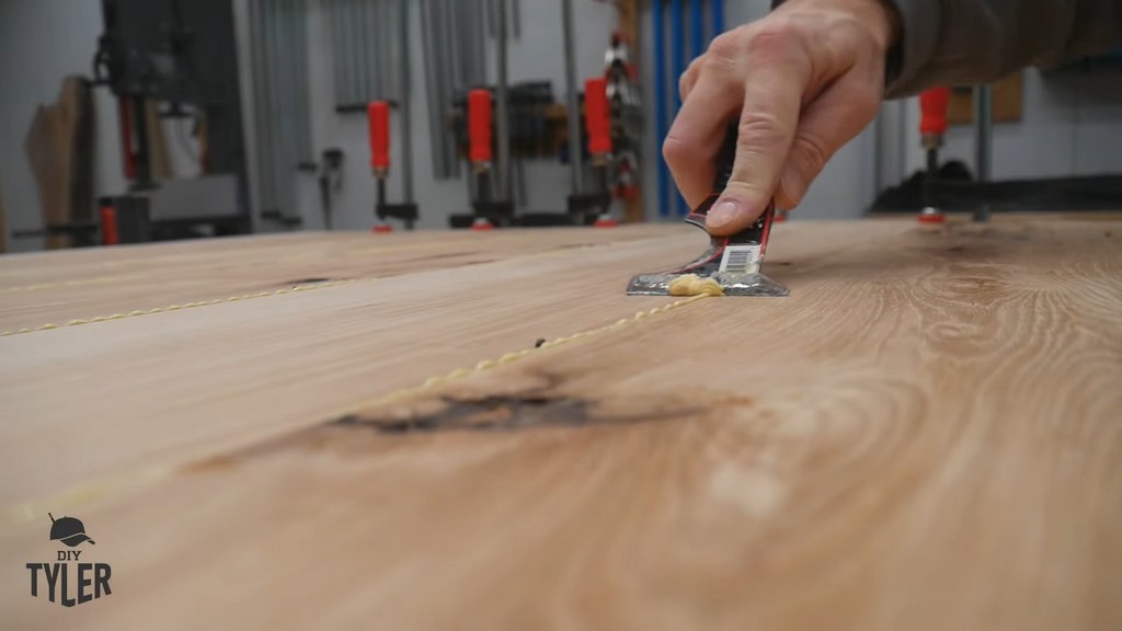 man scraping excess wood glue off of hickory board slab