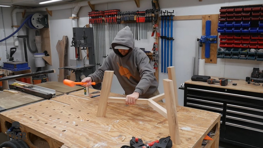 man using mallet to install angled table legs onto tripod joint table brace