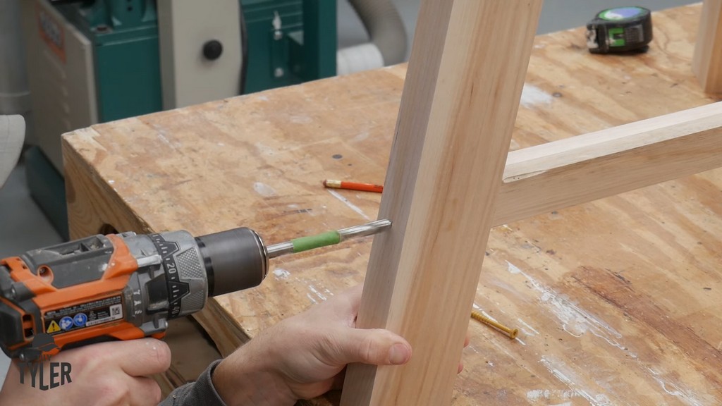 man drilling dowel hole into angled table leg and tripod joint brace