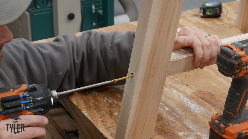 man fastening screw into angled table leg and tripod joint brace