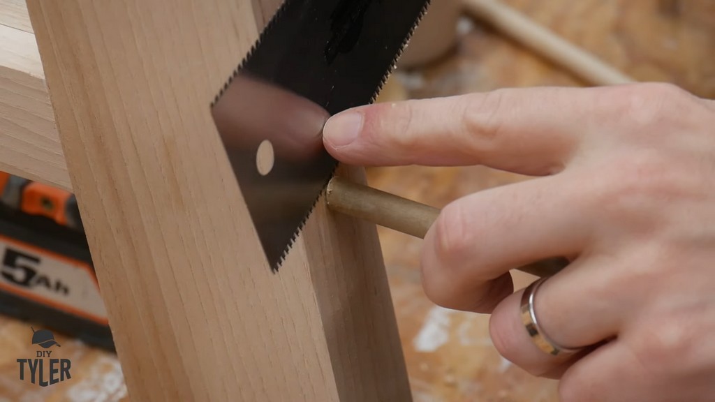 man using saw to cut off excess piece of wooden dowel