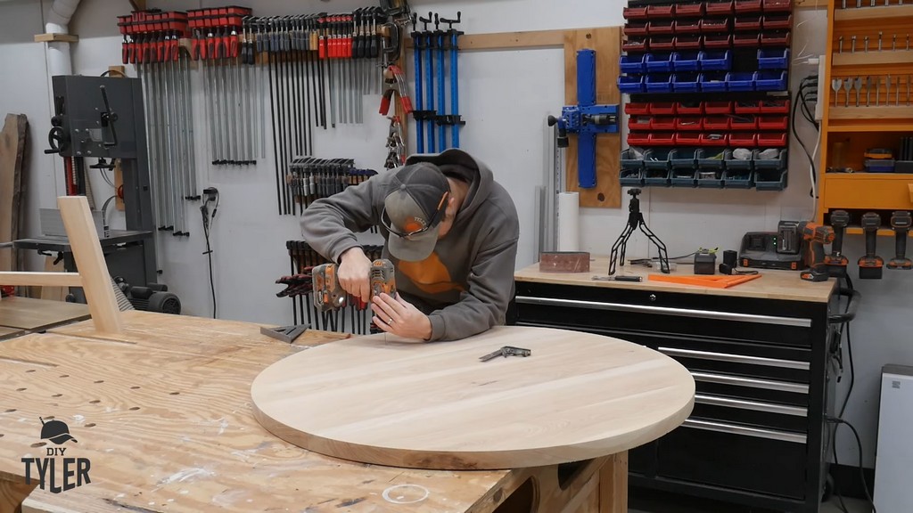 man drilling pilot holes into bottom of tabletop for DIY round coffee table
