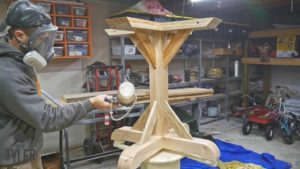 man applying spray finish to pedestal game table