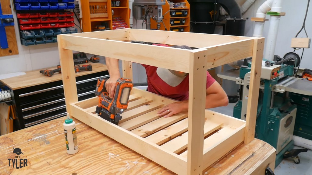 man using nail gun for bottom slats of DIY deck fire table frame