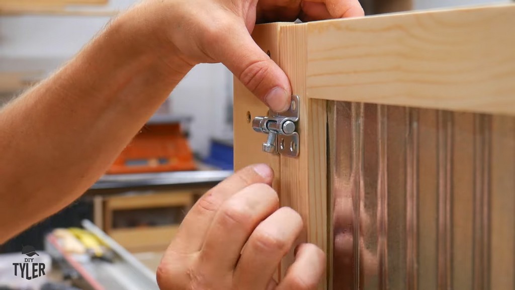 man installing latch for door on side of DIY deck fire table frame