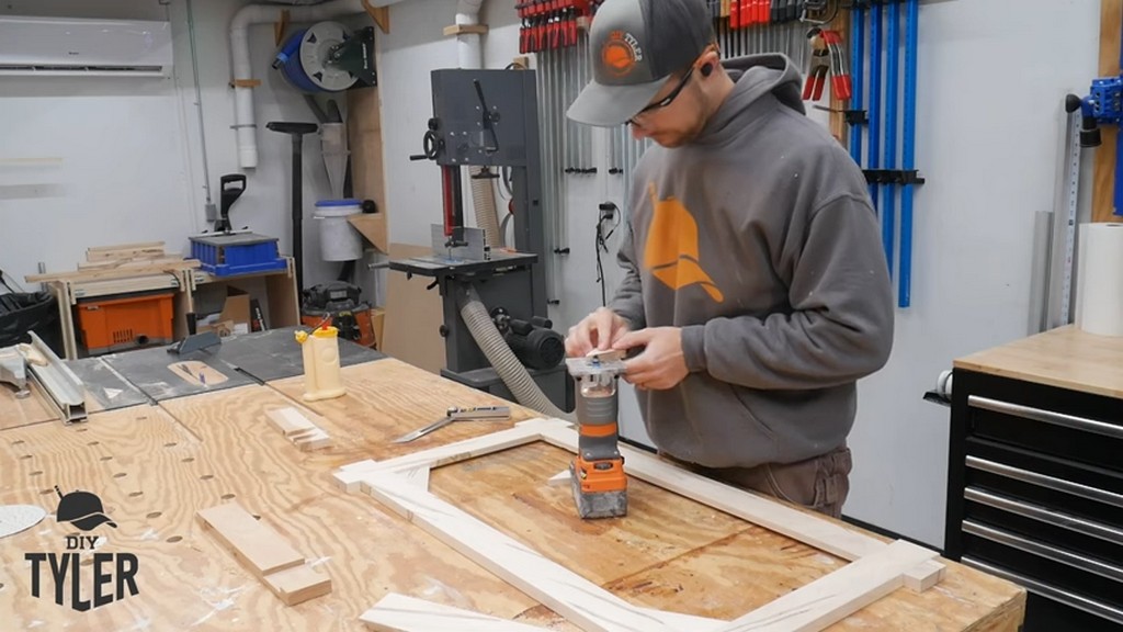 man using roundover router bit on edge of corner piece for picture frame